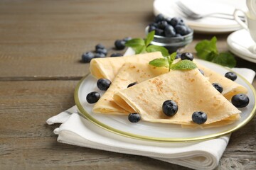 Tasty crepes with blueberries and mint on wooden table, closeup. Space for text