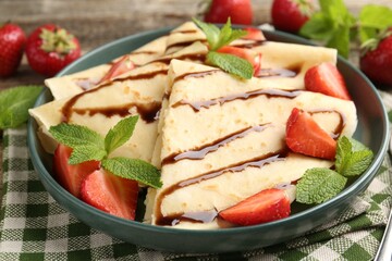 Tasty crepes with strawberries, chocolate sauce and mint on wooden table, closeup