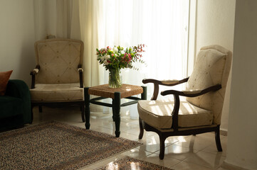 Sunlit living room featuring two elegant armchairs, a woven table, and a vibrant floral arrangement, creating a warm and inviting atmosphere