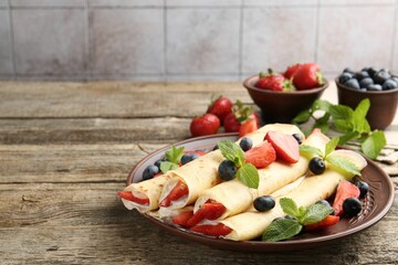 Tasty crepes with berries, cream and mint on wooden table, closeup. Space for text