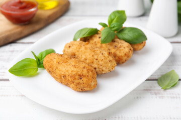 Tasty fried croquettes and basil on white wooden table, closeup