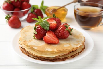 Delicious crepes with strawberries, honey, mint and tea on white wooden table, closeup