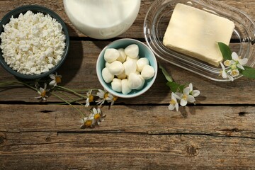 Different fresh dairy products and flowers on wooden table, flat lay. Space for text