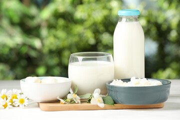 Different fresh dairy products and flowers on white wooden table outdoors