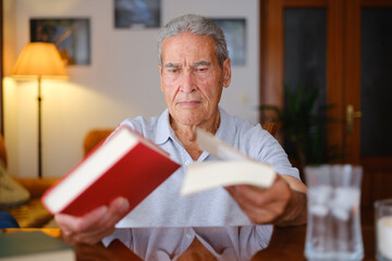 Senior man choosing between two books at home