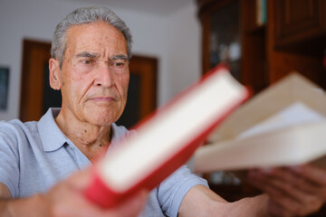 Close-up of an older man thoughtfully examining a book at home.