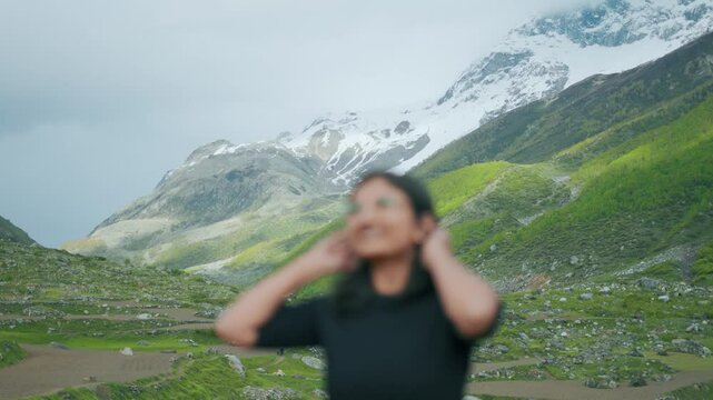 4K shot of defocused girl looking at mountain valley in Sural Bhatori, Pangi Valley, India. Happy tourist exploring hidden gems. Summer mountains with snow peaks and dark clouds in sky. Travel concept