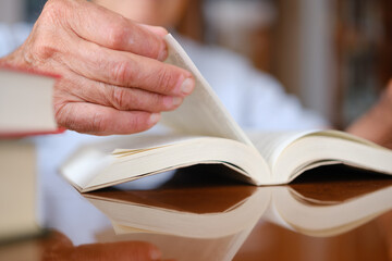 Old man turning the page of a book, with focus in his hands and reflection.