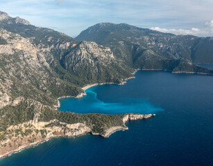 Captivating aerial view showcasing a beautiful coastal landscape with rugged mountains, lush greenery, and serene blue waters under a clear sky