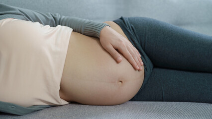 A close-up view of a pregnant woman lying on her side on a sofa, gently holding her bare belly in a peaceful and relaxed setting.