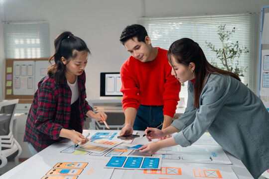 Group of young professionals engaging in a collaborative brainstorming session for a mobile app design project. They are focused on creating innovative user interface solutions