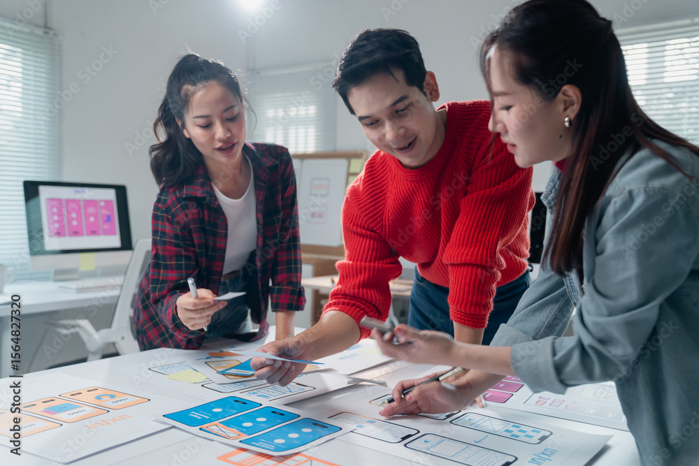 Poster three asian ux designers working together on developing an app interface wireframe for a mobile appl