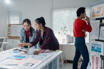 Two ux/ui designers analyzing wireframes and prototypes for a new mobile app while a third designer...