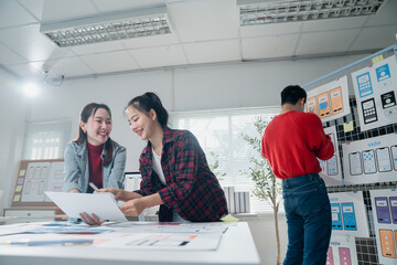 Two asian female ux designers smiling and collaborating on a new project for a mobile app interface...