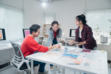 Three Asian UI/UX developers collaborating on mobile app design in a modern office, using desktop...