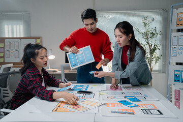 Creative team actively engaged in designing a mobile app interface, using printed wireframes and...