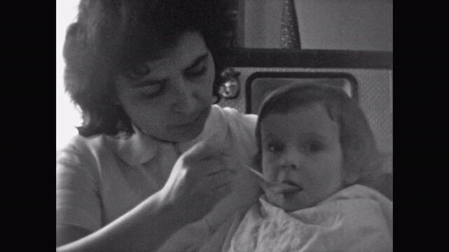 Archive film, Mother feeding baby home-cooked food, close up. Parent holding little girl child, feed with spoon on vintage home background. Home family routine. Vintage old Archival retro 1960s