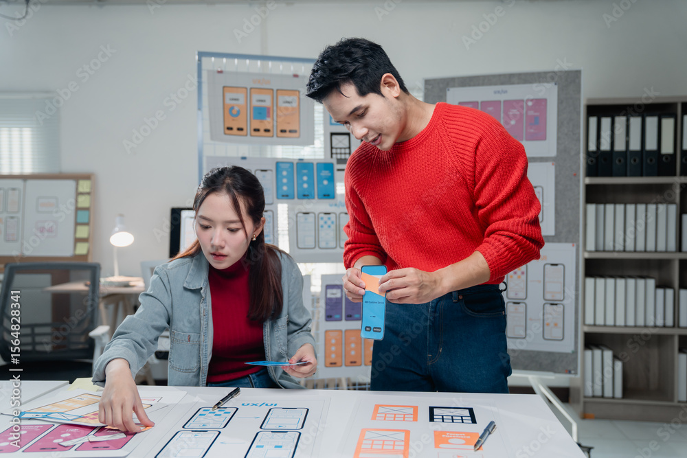 Poster two designers working together on a mobile app project, examining wireframes and prototypes. they ar