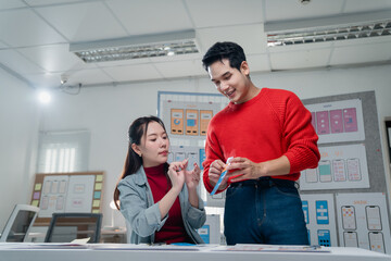 Two asian ux designers are working together comparing layouts for mobile app interfaces in their...