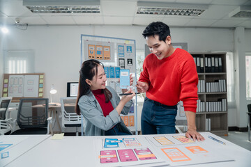 Two young UX designers collaborating on mobile app interface wireframes, engaging in discussion...