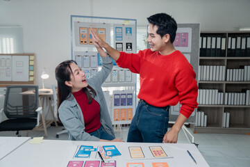 Two enthusiastic UI/UX designers sharing a high-five, celebrating their successful collaboration on...