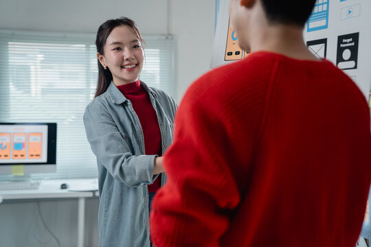 Two young web designers engaging in a discussion about user interface design while showcasing a new mobile application prototype in a modern office setting