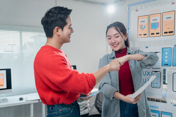 Two young asian ux/ui designers fist bumping and smiling after successfully completing a project,...