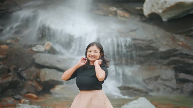 4K Portrait of teenager Indian girl against waterfall in Sural Bhatori, Pangi Valley, India. Tourist exploring mountains during summer season. Travel and freedom. Young woman Travel.