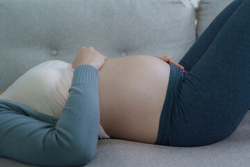 Pregnant woman lying on a couch with hands on her belly, dressed in comfortable clothes, conveying calmness, care, and maternal anticipation.