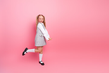 Happy schoolgirl posing against pastel pink background wearing formal uniform with joyful expression