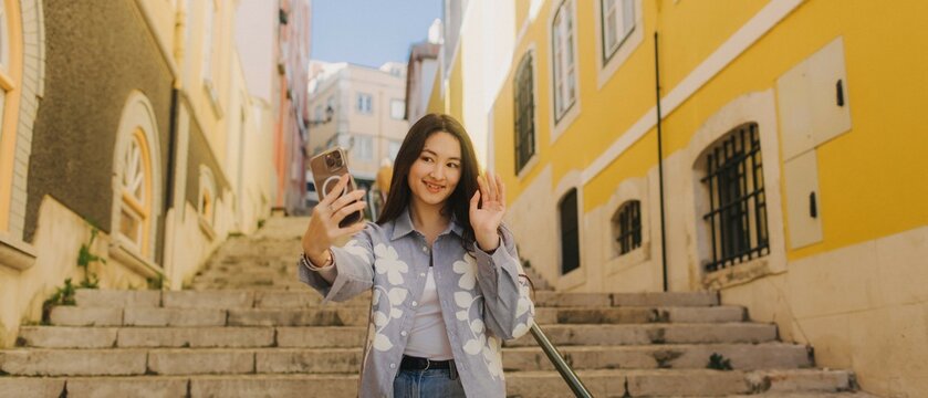 Vlogger traveler girl recording video on phone share via app her travel vacation in the Lisbon. Woman influencer shooting social media stories on the street leading. UGC. Part of a series