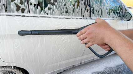 Two hands wielding a foamy spray lance at a white sedan, cleansing ritual, sumptuous suds, car care...