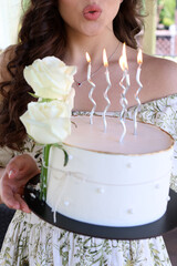 Holding a cake in her hands, a girl blows out the candles. Birthday celebration.