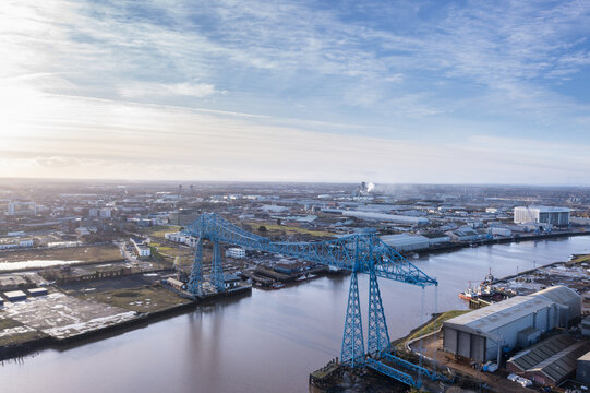 Aerial view of the iconic blue Middlesbrough Transporter Bridge spanning the tranquil river under a vast sky, Stockton-on-Tees, England, United Kingdom.