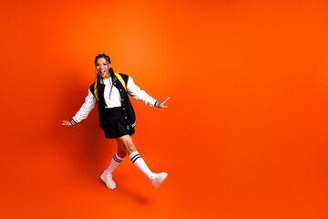 Dynamic teenager in stylish jacket posing joyfully against vibrant orange backdrop representative of a lively lifestyle.