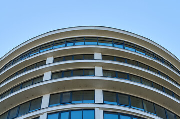 A distinctive building showcases rounded balconies and large windows under a bright blue sky, emphasizing modern design.