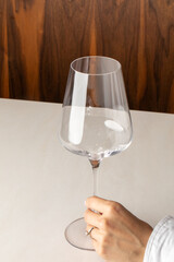 A delicate hand of a South Asian woman elegantly cradles an empty wine glass, echoing silent celebrations of Amontillado Day and the esoteric Feast of Bacchus