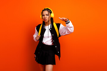 Young teen girl with headphones posing creatively against vibrant orange background, highlighting...