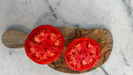 Sliced ruby tomatoes on rustic olive wood evoke Mediterranean harvest, summer solstice festivities,...