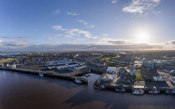 Aerial view of the Amble harbor where the Coquet River meets the North Sea, the town nestled inland under a sun-drenched sky, Morpeth, England, United Kingdom.