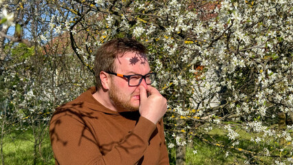 A contemplative Caucasian man in an orchard battles spring allergies, embodying the dance of Hanami...