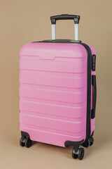 Angled side view of pink suitcase on beige background, concept modern travel luggage portability