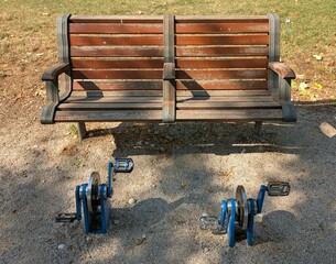 Banco de madera con aparatos de pedaleo en un parque público.