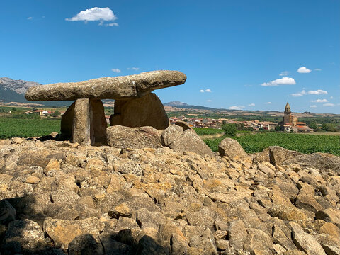The Whitch's Hut dolmen, Elvillar, La Rioja, Alava, Spain, ancient stone dolmen in a rocky landscape with a village and mountains in the background.