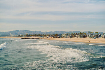 Ocean waves gently meet the sandy shore with distant mountains under a blue sky. Los Angeles, USA