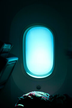 Airplane window with bright blue sky, seat and interior visible in low light. Los Angeles, USA