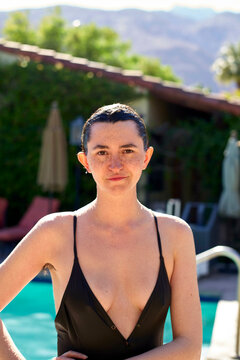 Young adult woman by a poolside with mountains in the background, wearing a black swimsuit. Palm Springs, USA
