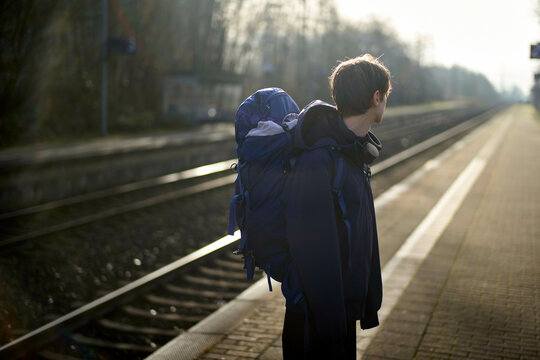 A person with a large backpack stands on an empty train platform under a cloudy sky. Weser Uplands, Germany
