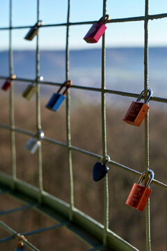Colorful love locks attached to a wire fence with a blurred natural landscape in the background. Weser Uplands, Germany