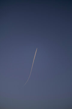 A single contrail streaks across a clear blue sky, creating a gentle curve behind the airplane. Weser Uplands, Germany